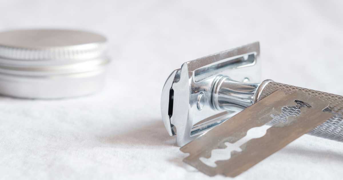 Close-up image of silver safety razor, blade and lip-balm tin.